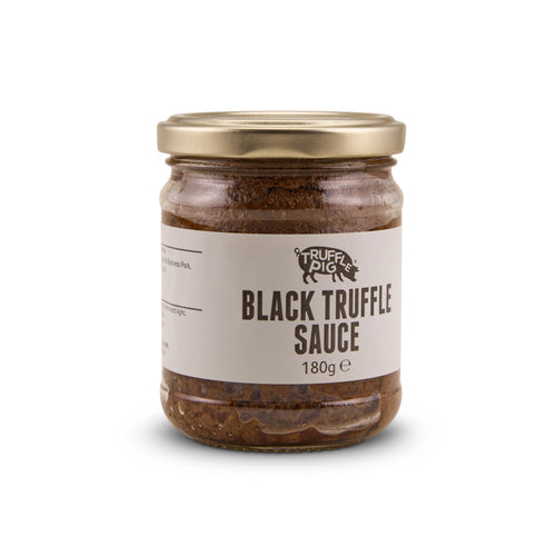 A glass jar of Truffle Pig's Black Truffle sauce 180g with a gold lid and a beige label, set against a plain white background.